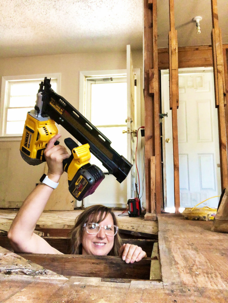 pretty handy girl in crawlspace with framing nailer extended over head
